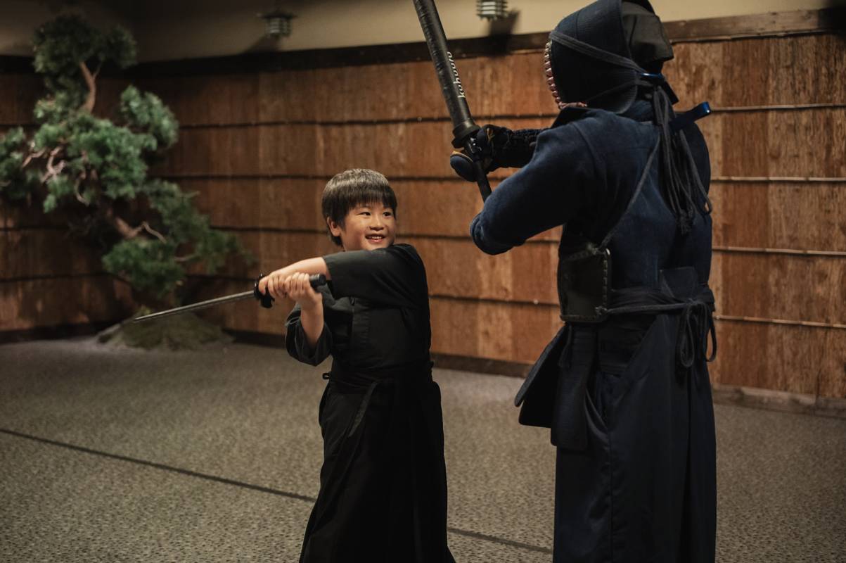 Child practicing a sword strike on the samurai-shaped striking target under supervision